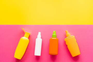 Top view of bottles of sunscreens on yellow and pink background.