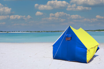 A tourist tent stands on the white sand on the beach. Summer tent for family outdoor recreation. camping, summer. Blue-yellow fabric. Active rest, family leisure away from civilization	