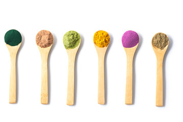 Superfood powders: sweet potato, matcha, spirulina, hemp, turmeric, carob in wooden spoons on a white background, flat lay, top view.