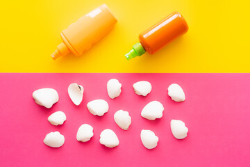 Top view of seashells near bottles of sunscreens on yellow and pink background.