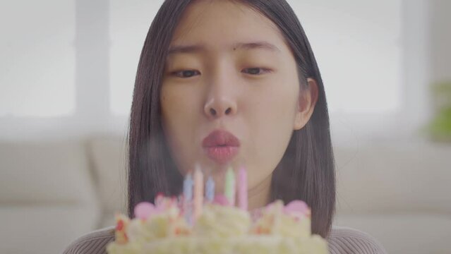 Portrait of attractive cheerful asian woman blowing candles on colored Happy birthday lettering during anniversary celebration. Happy asian girl during holiday at home.