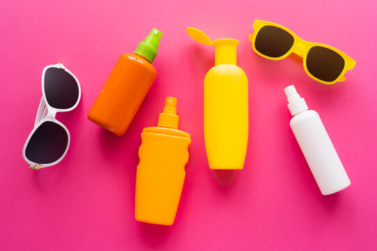 Top view of sunglasses and bottles of sunscreens on pink surface.