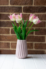 Vase with tulips on a white table. Flowers on the background of a brick wall