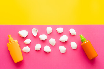 Top view of white seashells near sunscreens on yellow and pink background.