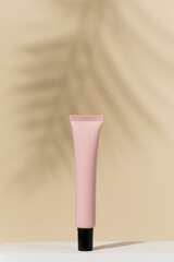 Anti-aging under eye lotion blank tube on beige background with palm leaf shadow