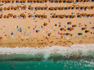 Aerial view of an emerald and transparent Mediterranean sea with a white beach full of beach umbrellas and tourists who relax and take a bath.