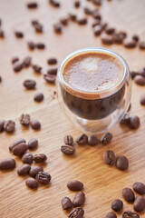 A transparent glass cup of hot espresso standing on a wooden table top
