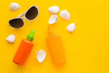 Top view of sunglasses near sunscreens and seashells on yellow background.