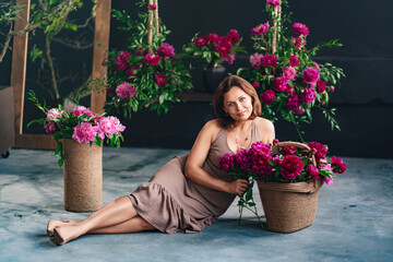 a woman sits on a podium near a basket of peonies and collects a bouquet.