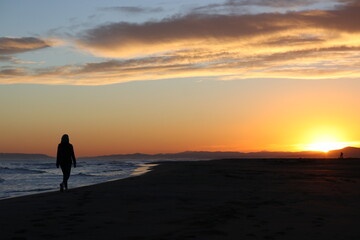 silhouette of person walking on the beach at sunset 