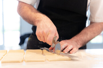 Detail of the hands of a man cooking croissants, measuring the puff pastry and making cuts, work at home