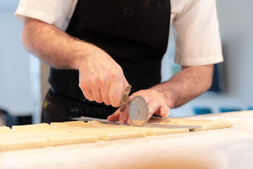 Detail of the hands of a man cooking croissants, measuring the puff pastry and making cuts, work at home