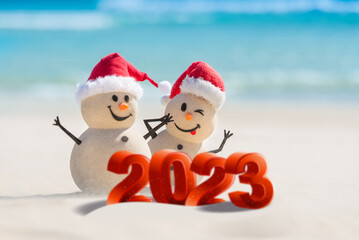 Two Sandy Snowmen are celebrating the New Year on a beautiful beach with 2023 3d text, concept for...