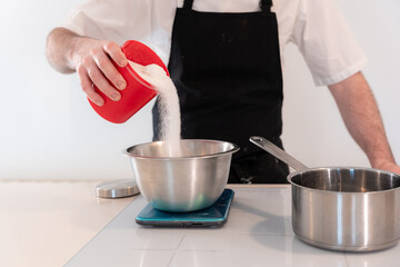 Hands of a man cooking a red velvet cake at home, preparing Swiss meringue with egg whites in a...