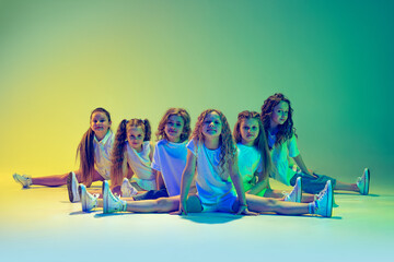 Group of children, little girls in sportive casual style clothes dancing in choreography class isolated on green background in yellow neon light. Concept of music, fashion, art