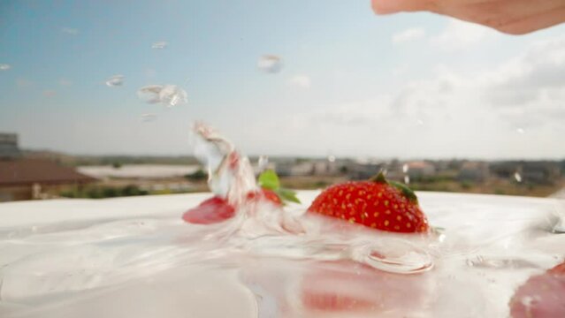 Throw a handful of strawberries into the water against the blue sky. close-up. slow mo