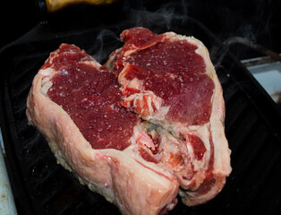 red raw sirloin steak being grilled on iron cast during day-time family lunch on a weekend