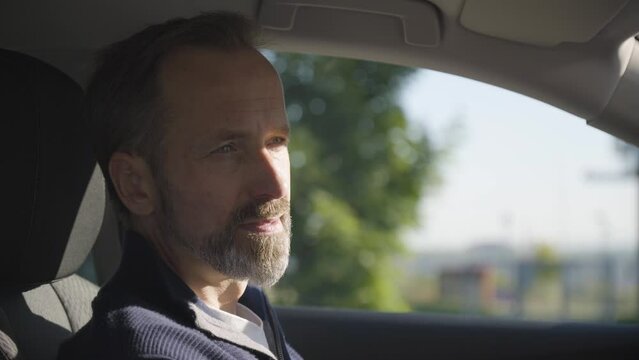 A middle-aged handsome Caucasian man looks around in thought in a car - side closeup