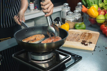 Woman chef salts raw salmon steak in a frying pan. Healthy seafood. Chef preparing salmon steak on stove. Cooking food concept.