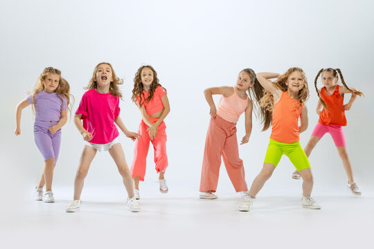Dance group of happy, active little girls in bright colorful clothes dancing isolated on white studio background. Concept of music, fashion, art, childhood, hobby
