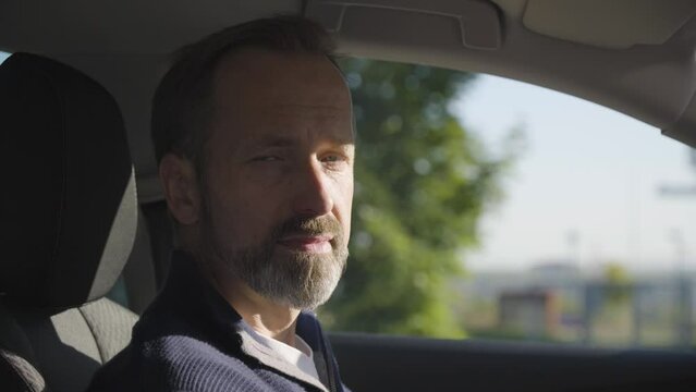 A middle-aged handsome Caucasian man looks seriously at the camera in a car - closeup