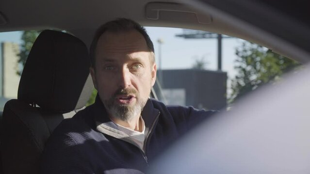 A middle-aged handsome Caucasian man talks to the camera with anger in a car - closeup