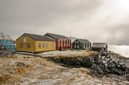 Flatey, Iceland, May 5, 2022: Houses on a cliff, painted in primary colors under a dark sky on which the sun breaks through