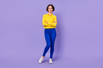 Full size photo of nice young lady crossed arms wear yellow shirt pants sneakers isolated on violet...