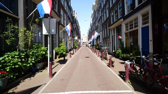 Beautiful street in Amsterdam, with Netherlands flags displayed on typical dutch buildings. Old centre district and typical architecture in Holland.