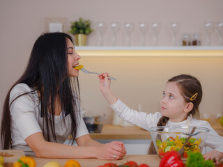 Happy mother and daughter enjoy prepare freshly salad together in kitchen. Healthy food at home. Healthy Lifestyle and Eating Concept. little influencer filming blog about healthy eating