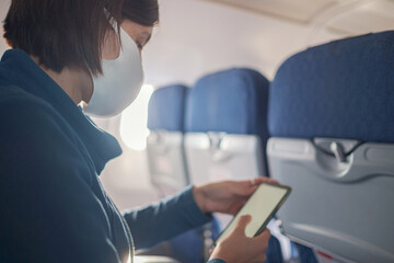 Naklejka na ściany i meble Young beautiful woman sitting at window of plane during the flight. new normal travel after covid-19 pandemic concept. shows smartphone monitor screen, mock-up
