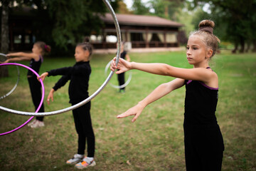 Girl doing exercise with hoop on rhythmic gymnastics training with other trainees outdoors in sports camp in summer