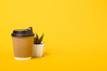 Disposable paper cup of coffee and plant on orange background, copy space. Takeaway coffee.