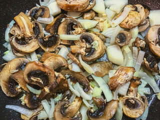 Fried mushrooms in cast iron pan on wooden background with copy space, top view