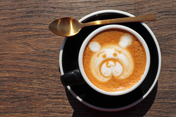 Latte art, drawing of the bear’s face, coffee art made by barista with a golden spoon on wooden background table, view from above or top. Copy space for text on the left side. 