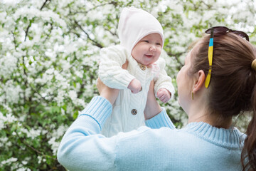 Happy Mother and newborn daughter stands in the garden blooming apple trees and having fun outdoors in springtime season, closeup