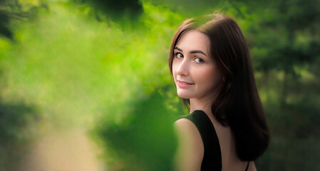 Young beautiful woman portrait in dress looks at camera from green blurry background in park for banner.