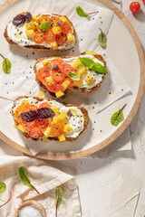 Italian bruschettas with roasted tomatoes, cream cheese, pineapple slices and herbs on a kitchen countertop. Prepared to serve