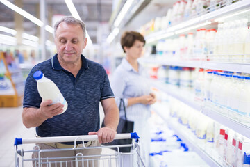 elderly retired man buying milk in dairy section of the supermarket