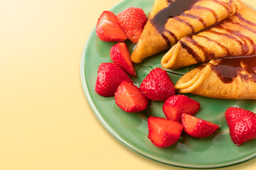 Delicious thin pancakes with fresh strawberry pieces and chocolate, on a green plate. Place for text. Close-up