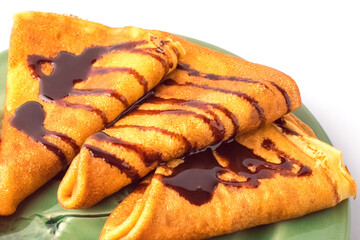 Thin pancakes with chocolate, on a green plate. Close-up