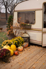 Autumn camping. The trailer is decorated with autumn flower, pumpkins, decor. Wooden chair placed...