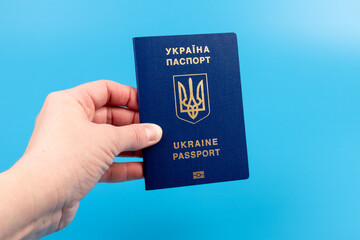 Passport of a citizen of Ukraine in a female hand on a blue background, close-up. Inscription in Ukrainian Ukraine Passport