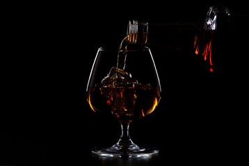 Pouring whiskey drink into glass with ice cubes on dark background