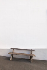 Old wooden bench stands alone in front of a sloping white wall. Sloping background floor. Alte...