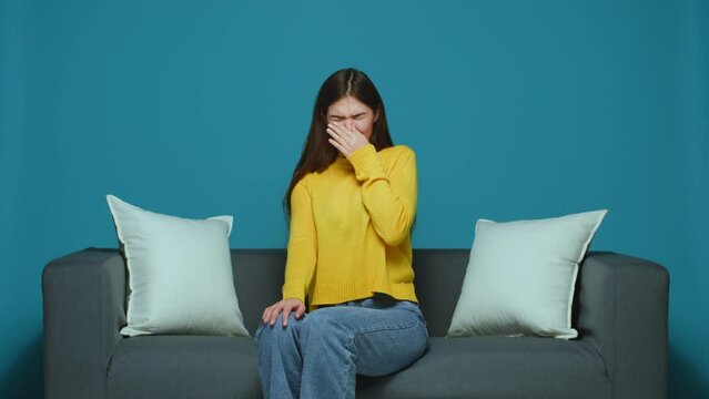 Bad smell. Young modern girl cover pinching nose with hands to avoid stink, intolerable disgusting odor, sitting on sofa