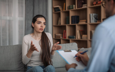 Unhappy sad emotional european millennial woman client talking to psychologist guy in clinic