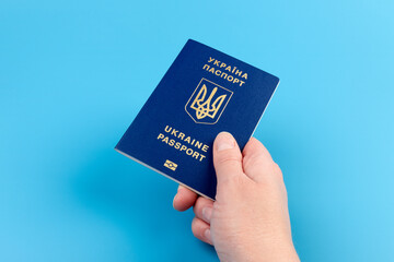 Passport of a citizen of Ukraine in a female hand on a blue background, close-up. Inscription in Ukrainian Ukraine Passport