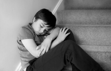 Black and White portrait Sad boy sitting alone on staircase, Lonely kid looking dow with sad face not happy to go back to school, Depressed child boy sitting in the corner of a stair,Mental health