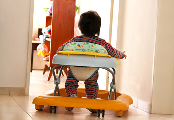 Baby walker. Roller walker training car. 
Baby learning to walk in infant walker. Learning. Baby walker with wheels and safety measures.  
Little girl. Discovery.   - obrazy, fototapety, plakaty